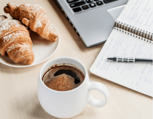 work station with laptop, croissants, hot cocoa, and a journal