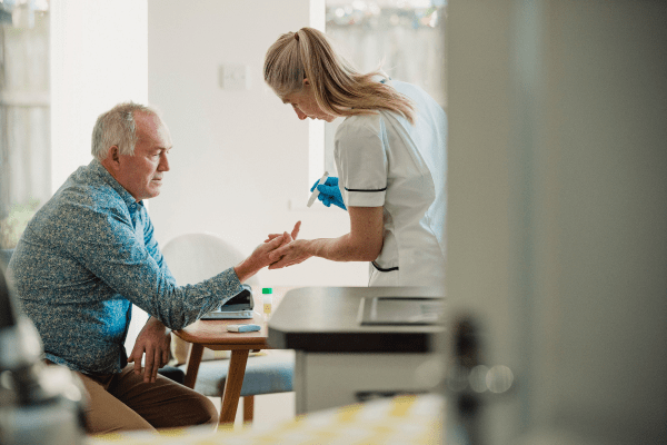 Nurse helping elderly man with glucose monitor 