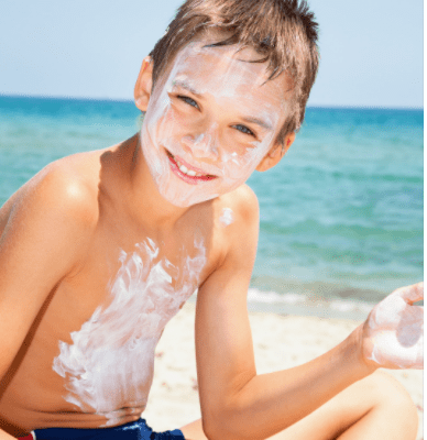 child sitting on the beach with sunscrreen on face and stomach