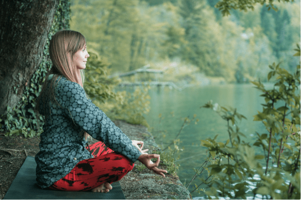 woman sitting in meditation pose by the bank of a river